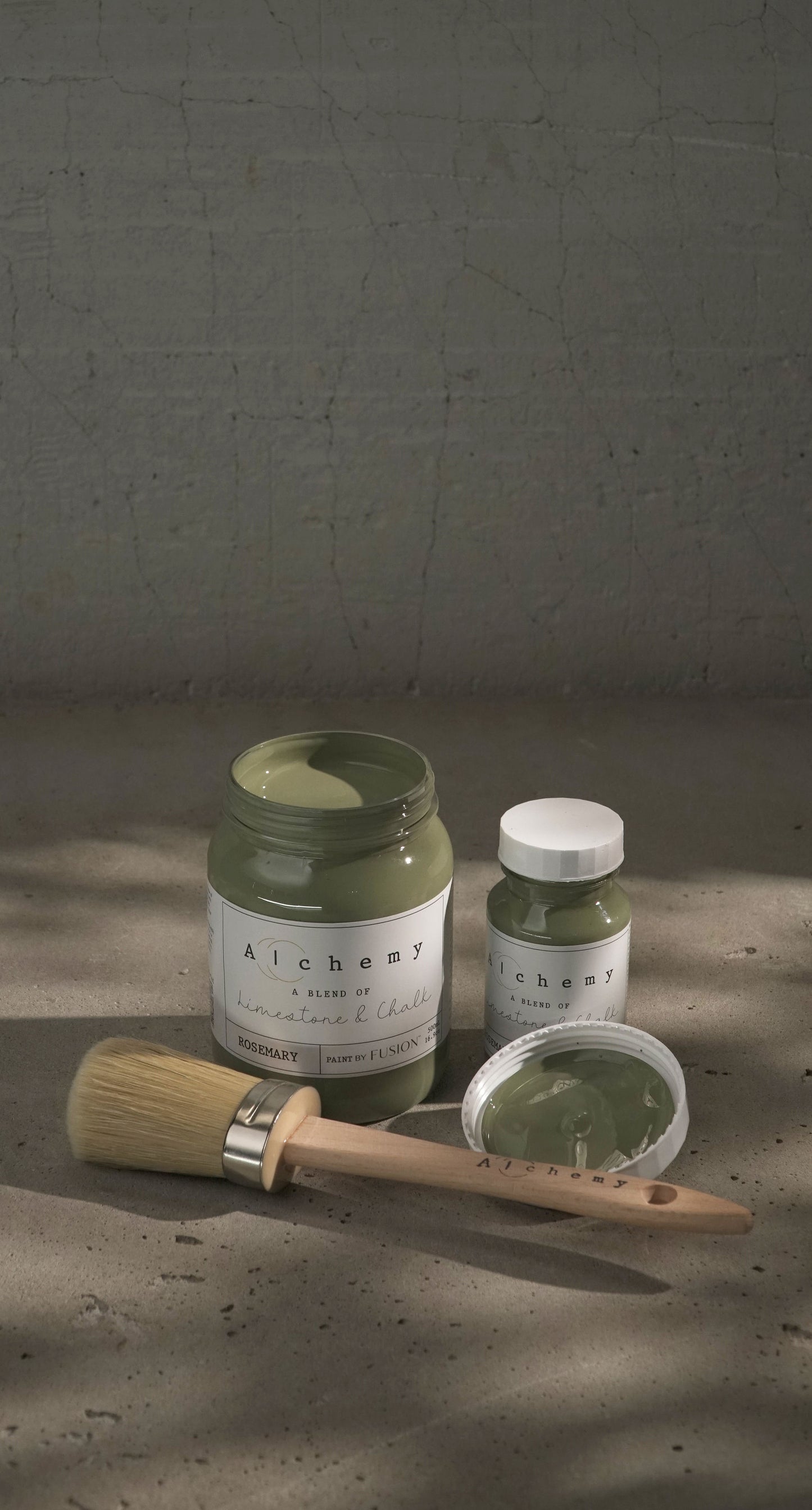 Botes Alchemy by Fusion Rosemary 500ml y 120ml abiertos con brocha sobre fondo de cemento texturizado con luz lateral, pintura a la tiza verde herbáceo limestone y chalk