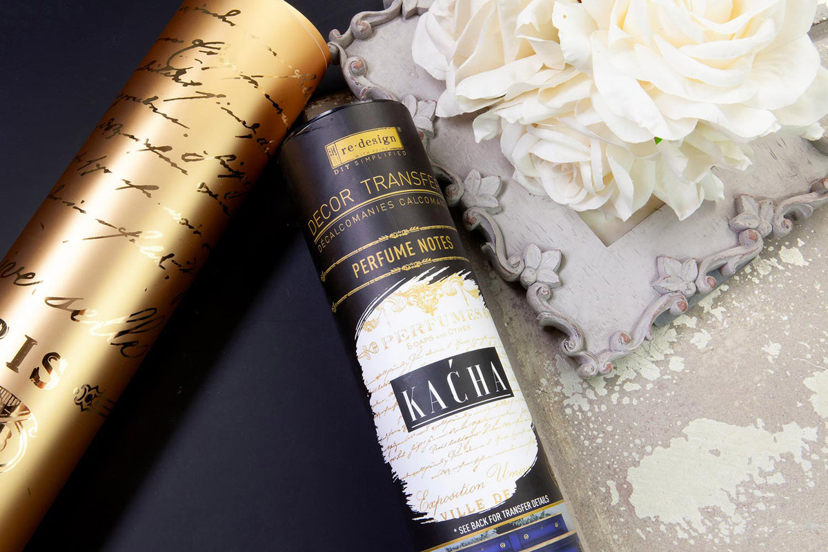 Packaging Gold Foil Decor Transfer Perfume Notes de Kacha - tubo Re-Design with Prima negro y dorado con lámina dorada enrollada y rosas blancas sobre bandeja barroca gris