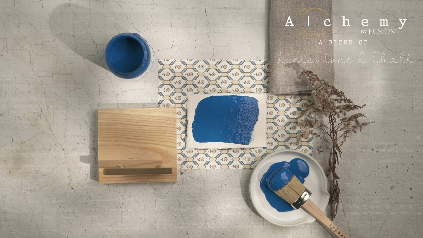 Flatlay inspiracional Alchemy by Fusion Ocean con muestra de color azul marino, bote 120ml, brocha y elementos naturales sobre fondo de azulejo