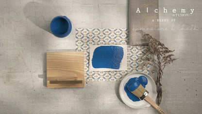 Flatlay inspiracional Alchemy by Fusion Ocean con muestra de color azul marino, bote 120ml, brocha y elementos naturales sobre fondo de azulejo
