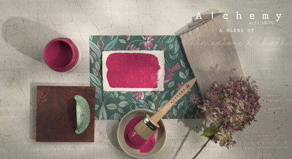 Flatlay inspiracional Alchemy by Fusion Raspberry con muestra de color fucsia, bote 120ml abierto, brocha redonda, tirador cerámico verde y hortensia seca sobre fondo de azulejo craquelado