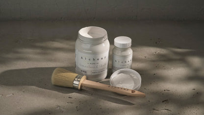 Botes Alchemy by Fusion Birch 500ml y 120ml con brocha redonda sobre superficie de cemento con luz natural, pintura a la tiza blanco roto terroso