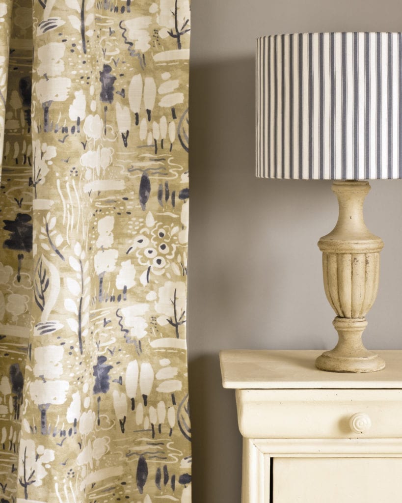 Composición decorativa con una mesita auxiliar pintada con Chalk Paint™ Cream de Annie Sloan, junto a una cortina Ticking en Old Violet y una pantalla en tono Dulcet