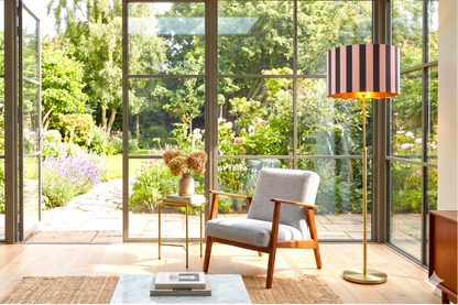 Pantalla cilíndrica artesanal rosa, azul y dorado irradiando luz cálida en rincón de salón – Anaqa Design